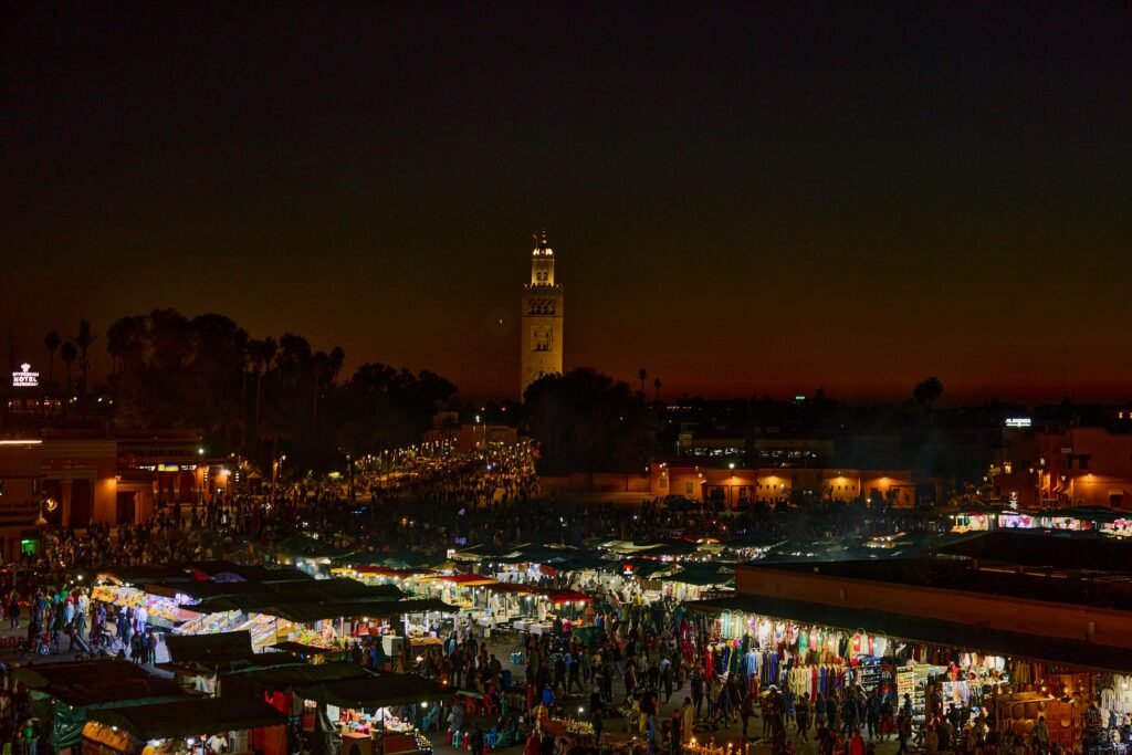 Voyages Spirituels au Maroc Experience the bustling night market in Marrakesh, Morocco, illuminated against a stunning twilight sky.