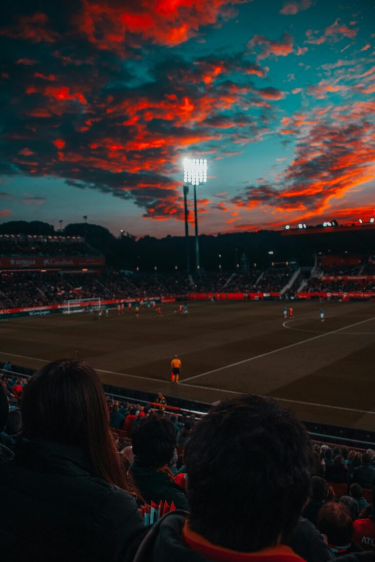Le Programme Sportif Dramatic sunset over a lively soccer game in a large stadium filled with spectators.