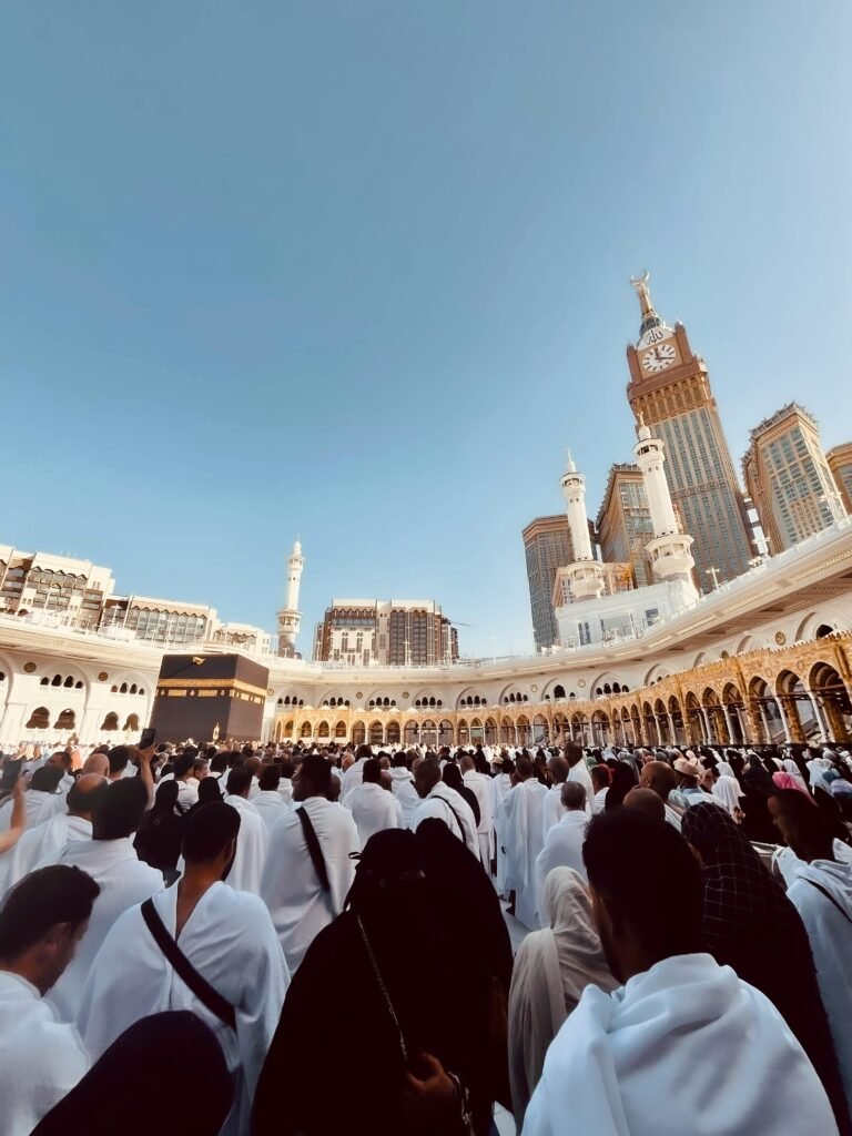 Nos voyages A large crowd of pilgrims at Masjid al-Haram in Makkah with the Kaaba and Abraj Al Bait Clock Tower visible.
